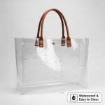 A stylish custom printed **clear pvc tote bag** with black webbing handles, filled with colorful retail items.