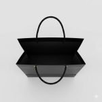 A luxury matte **black paper bag** with a gold foil stamped logo and black rope handles.