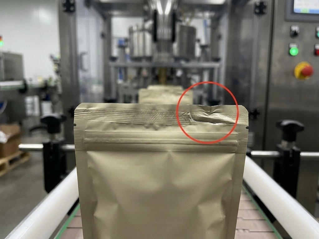 Close-up photograph of a snack food pouch with a wrinkled, failed top seal caused by material incompatibility on a high-speed production line.