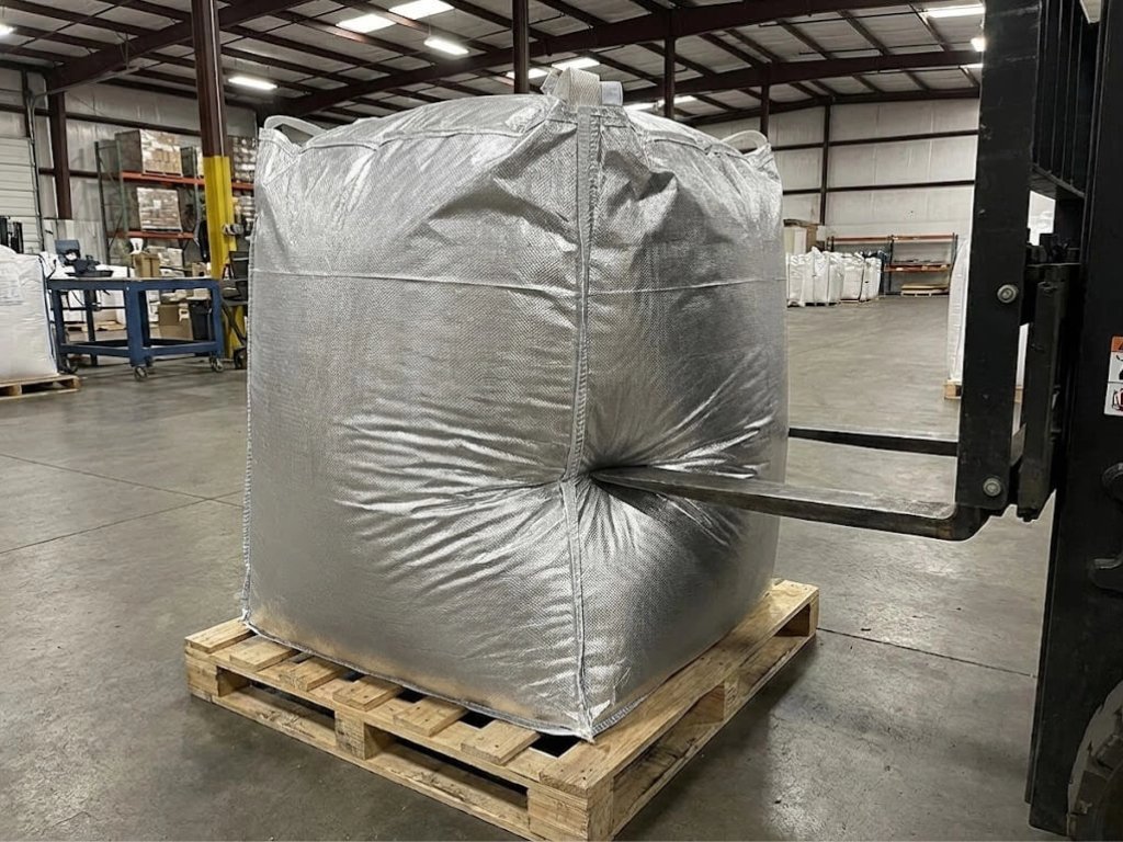 Large, reinforced aluminum foil bulk liner bag on a pallet in a warehouse, demonstrating mechanical durability by withstanding pressure from a forklift fork.