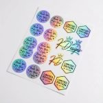 A custom die-cut holographic sticker showing a rainbow iridescent effect on a black package.