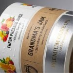 A roll of custom food labels with vibrant graphics being applied to glass juice bottles.