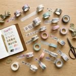 Several rolls of custom washi tape with various colorful floral and geometric patterns stacked on a wooden desk.