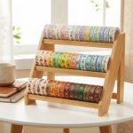 Several rolls of custom washi tape with various colorful floral and geometric patterns stacked on a wooden desk.