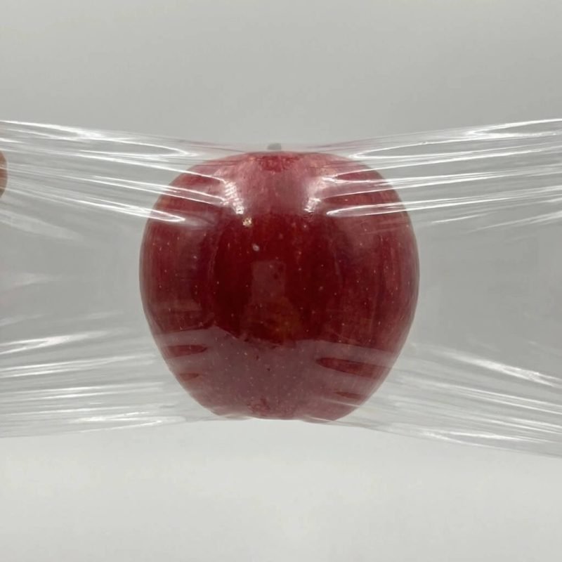 A clear POF film roll being applied to a bundle of retail gift boxes in a shrink tunnel machine.