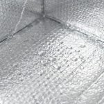 A silver insulated box liner being placed inside a brown corrugated shipping box filled with fresh meat and ice packs.