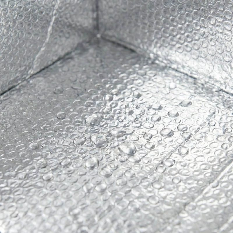 A silver insulated box liner being placed inside a brown corrugated shipping box filled with fresh meat and ice packs.