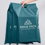 A blue poly mailer with handle featuring a custom white logo and being carried by its die-cut handle.