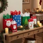 A group of Christmas paper bags in various sizes with reindeer and snowflake prints and red ribbon handles.