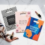 A group of small die cut paper bags with a matte black finish and a white custom jewelry logo.