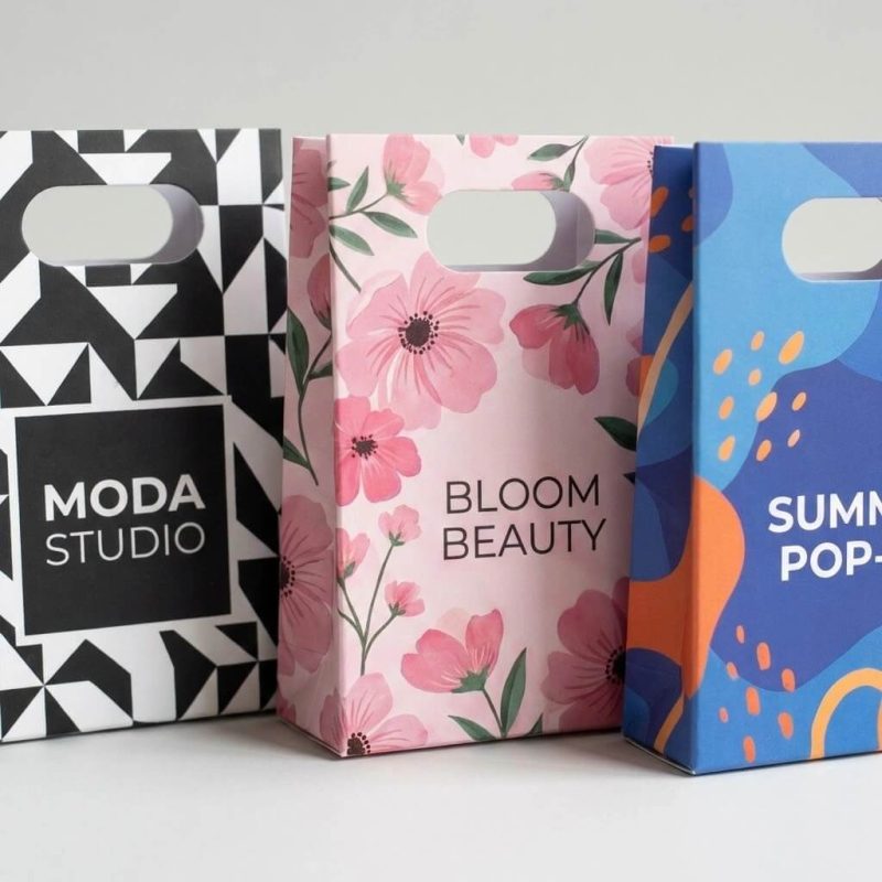A group of small die cut paper bags with a matte black finish and a white custom jewelry logo.