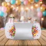 A silver pearlescent paper pillow box tied with a white ribbon and containing pink candies.