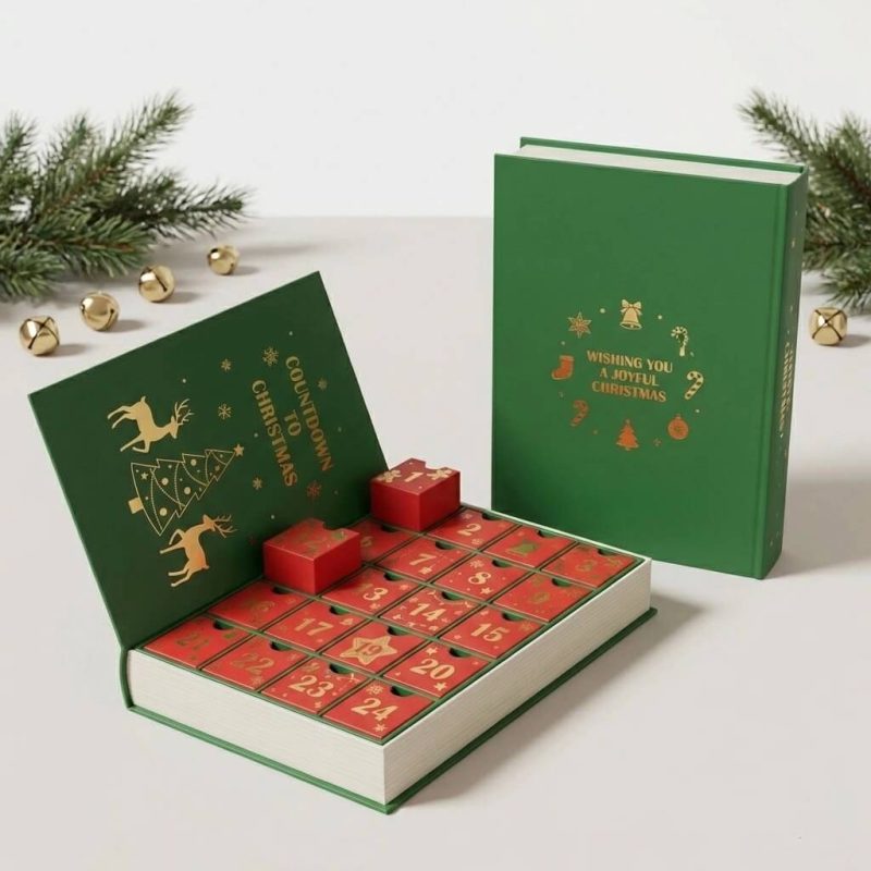A large book-shaped advent calendar box in festive red and gold with 24 small drawers pulled open to reveal beauty gifts.